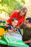 Happy Young Mixed Race Boy Enjoys A Toy Tractor While Parents Look On.