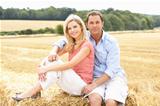 Couple Sitting On Straw Bales In Harvested Field