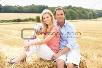 Couple Sitting On Straw Bales In Harvested Field