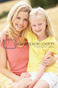 Mother And Daughter Sitting On Straw Bales In Harvested Field