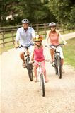 Family Cycling In Countryside Wearing Safety Helmets