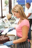 Woman Working Behind Counter In Caf Slicing Cake