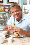 Male Customer Enjoying Sandwich And Coffee In Caf