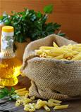 Linen bag of pasta (penne) and a bottle of oil on wooden table