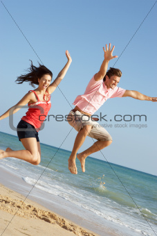 Young Couple Enjoying Beach Holiday Jumping In Air