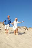 Senior Couple Enjoying Beach Holiday Running Down Dune