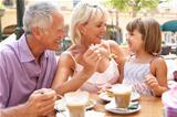 Grandparents With Granddaughter Enjoying Coffee And Cake In Caf
