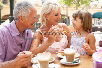 Grandparents With Granddaughter Enjoying Coffee And Cake In Caf