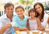 Young Family Enjoying Cup Of Coffee And Cake In Caf Together