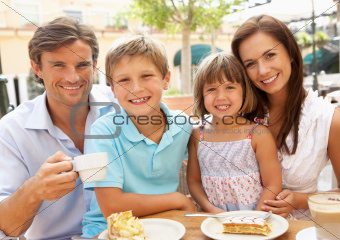 Young Family Enjoying Cup Of Coffee And Cake In Caf Together