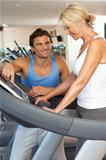 Senior Woman Working With Personal Trainer On Running Machine In Gym
