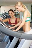 Woman Working With Female Personal Trainer On Running Machine In Gym