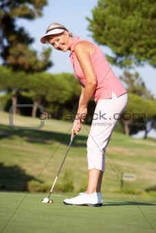 Senior Female Golfer On Golf Course Lining Up Putt On Green