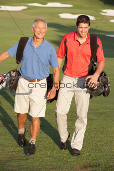 Two Men Walking Along Golf Course Carrying Bags
