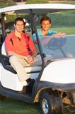 Two Male Golfers Riding In Golf Buggy On Golf Course