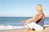 Senior Woman In Fitness Clothing Meditating On Beach