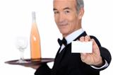 waiter carrying bottle of wine with glass and showing his personal card