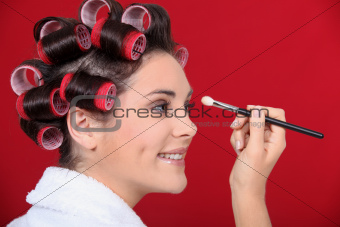 Woman with hair curlers applying make-up