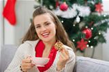 Happy young woman near Christmas tree with cup and cookie