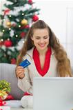 Happy young woman near Christmas tree making online purchases