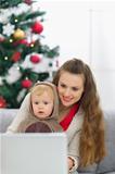 Mother and baby near Christmas tree using laptop