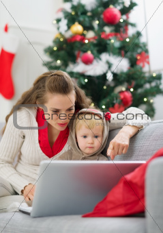 Mother showing baby something in laptop near Christmas tree