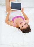 Happy young woman laying on bed with tablet PC