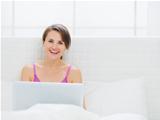 Happy young woman sitting on bed and working on laptop