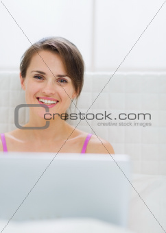 Portrait of happy young woman with laptop in bed