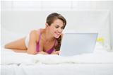 Happy young woman laying on bed and using laptop