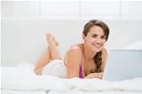 Happy young woman laying on bed and surfing internet