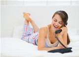 Happy young woman laying in bed and talking phone