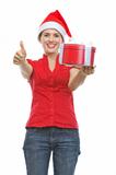 Smiling woman in Santa hat with Christmas present box showing thumbs up