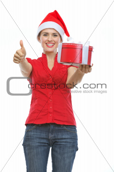 Smiling woman in Santa hat with Christmas present box showing thumbs up