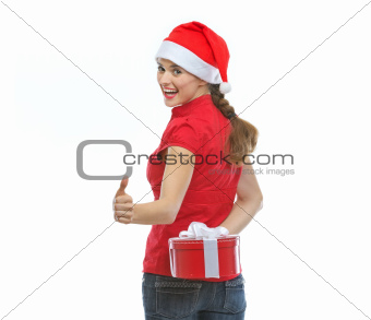 Woman hiding Christmas present behind back and showing thumbs up