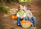 Adorable Brother and Sister Children Sitting on Wood Steps with Pumpkins Whispering Secrets or Kissing Cheek.