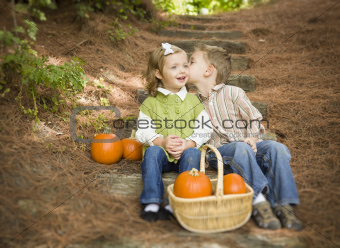 Adorable Brother and Sister Children Sitting on Wood Steps with Pumpkins Whispering Secrets or Kissing Cheek.