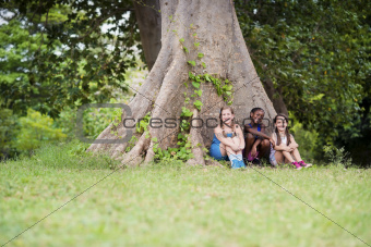 Three happy female friends sitting near big tree