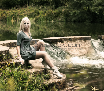 Beautiful Blonde Woman Sitting near the Waterfall