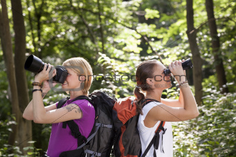 two women hiking in forest and looking with binoculars
