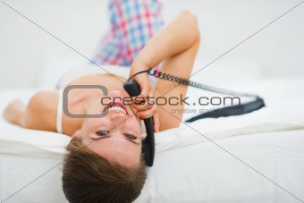 Happy young woman laying in bed and making phone call