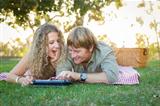 Playful Loving Couple Using a Touch Pad Computer at Their Picnic Outside.