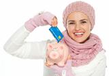 Happy woman in knit winter clothing putting credit card in piggy bank