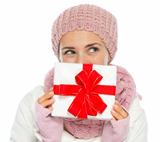 Thoughtful woman in knit winter clothing hiding behind Christmas present box