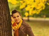 Thoughtful woman with fallen leaves leaning against tree