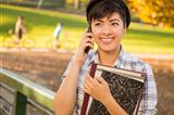 Outdoor Portrait of a Pretty Mixed Race Female Student Holding Books and Talking on Her Cell Phone on a Sunny Afternoon.