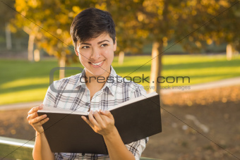 Portrait of a Pretty Mixed Race Female Holding Open Book Outdoors at the Park on a Sunny Afternoon.