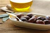 natural organic olives in a white bowl, a bottle of oil in the background