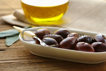 natural organic olives in a white bowl, a bottle of oil in the background