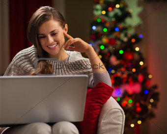 Happy woman looking in laptop in front of Christmas tree
